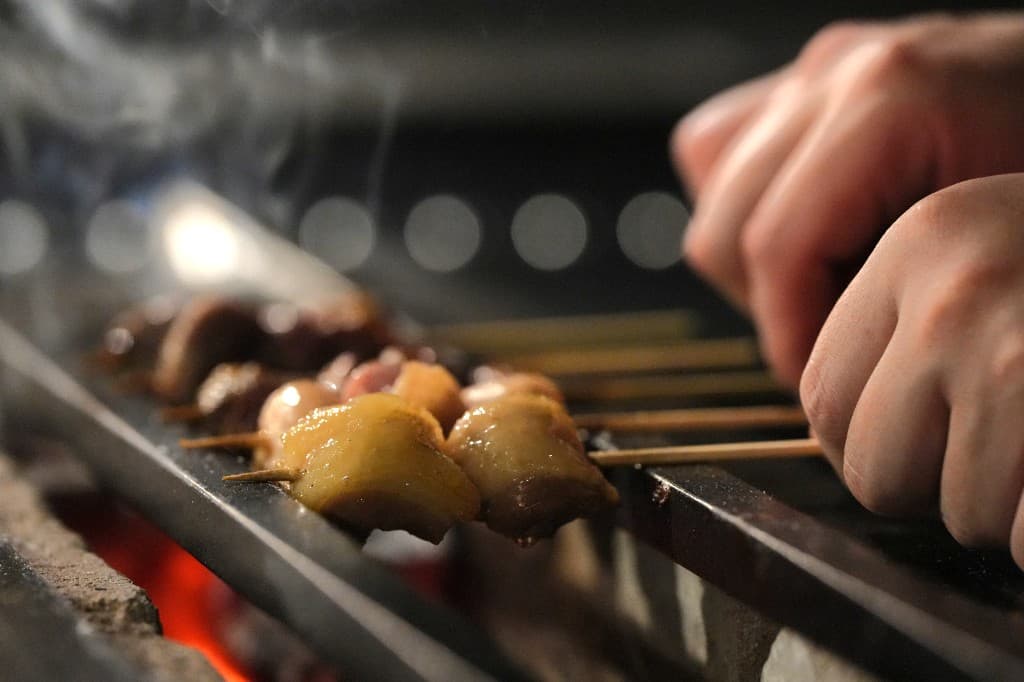 職人の手元で炭火にかけられる、艶やかな焼き鳥